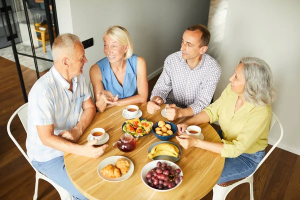 キッチンでテーブルの周りに座りながらランチを楽しむ陽気な高齢者のグループで高角図 コピースペース — ストック写真