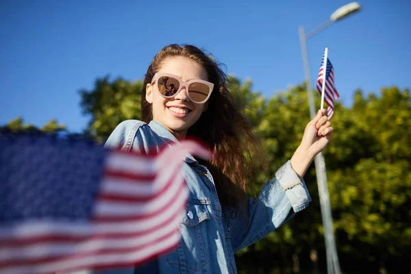 Mutlu heyecanlı güzel kız güneş gözlüğü kot ceket ulusal bağımsızlık günü geçit töreninde yürüyüş ve ulusal Amerikan bayrakları sallayarak giyiyor