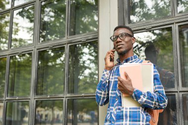 Kampüste açık havada telefonla konuşan çağdaş Afrikalı-Amerikalı öğrencinin bel kadar portre, kopya alanı