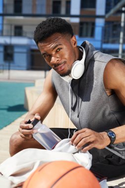 Açık basketbol sahasında dinlenirken kameraya bakan yakışıklı Afro-Amerikan adamın portresi, kopya alanı
