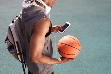 Basketbol tutan ve akıllı telefon açık havada kullanarak tanınmayan Afrikalı-Amerikalı adam yüksek açı portre, uzay arka plan kopyalamak
