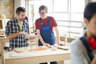 Atölyede gülümseyen genç çırak konuşurken dijital tablet kullanarak olgun marangoz portresi kadar Bel, kopya alanı