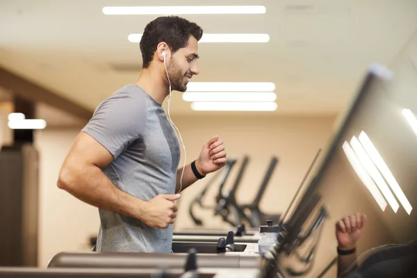 侧视图肖像英俊的年轻人在健身房的跑步机上跑步 微笑着享受锻炼 复制空间 — 图库照片