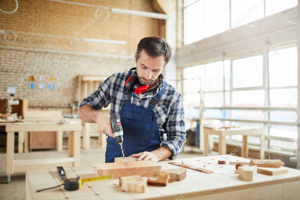 Waist up portrait of mature carpenter drilling wood while building handmade furniture in workshop, copy space