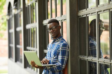 Üniversite kampüsünde açık havada poz veren dizüstü bilgisayar tutan akıllı Afrikalı öğrencinin portresikadar bel, kopya alanı