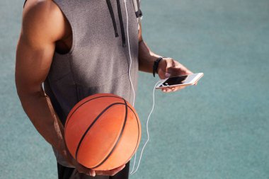 Basketbol tutan ve akıllı telefon açık havada kullanarak tanınmayan Afrikalı-Amerikalı adam orta bölümü, uzay arka plan kopyalamak