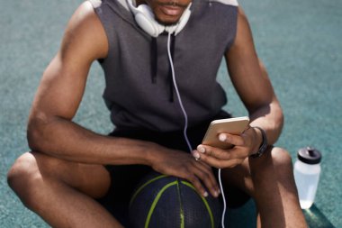 Basketbol sahasında otururken akıllı telefon kullanan çağdaş Afrikalı-Amerikalı adamın orta bölüm arka plan, kopya alanı