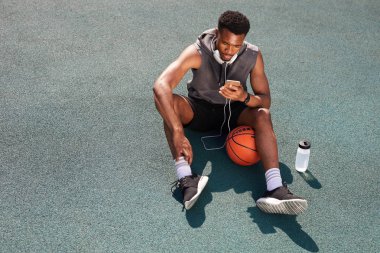 Basketbol sahasında oturan ve akıllı telefon kullanarak yakışıklı Afrikalı-Amerikalı adam yukarıda görünümü, kopya alanı