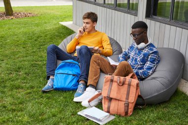 Kampüste fasulye torbaları üzerinde oturan açık havada rahatlatıcı iki öğrencinin yüksek açılı portre, kopya alanı
