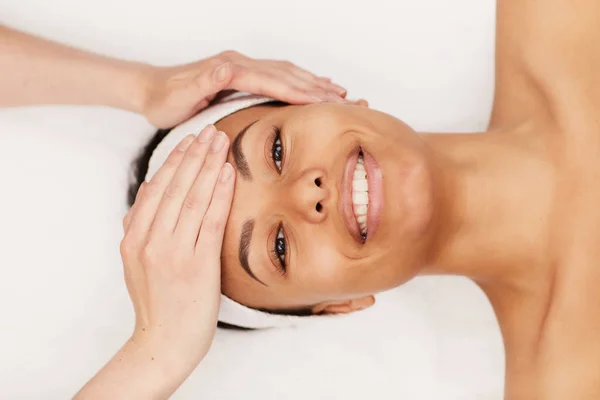 Top view portrait of beautiful mixed-race woman enjoying face massage in luxury spa, copy space