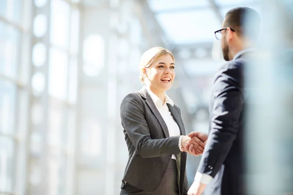 Positive confident young blond woman introducing yourself to businessman and making handshake with him