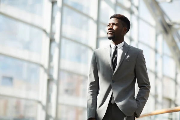 Serious pensive young Afro-American business corporation employee in gray suit holding hand in trousers pocket and looking into distance