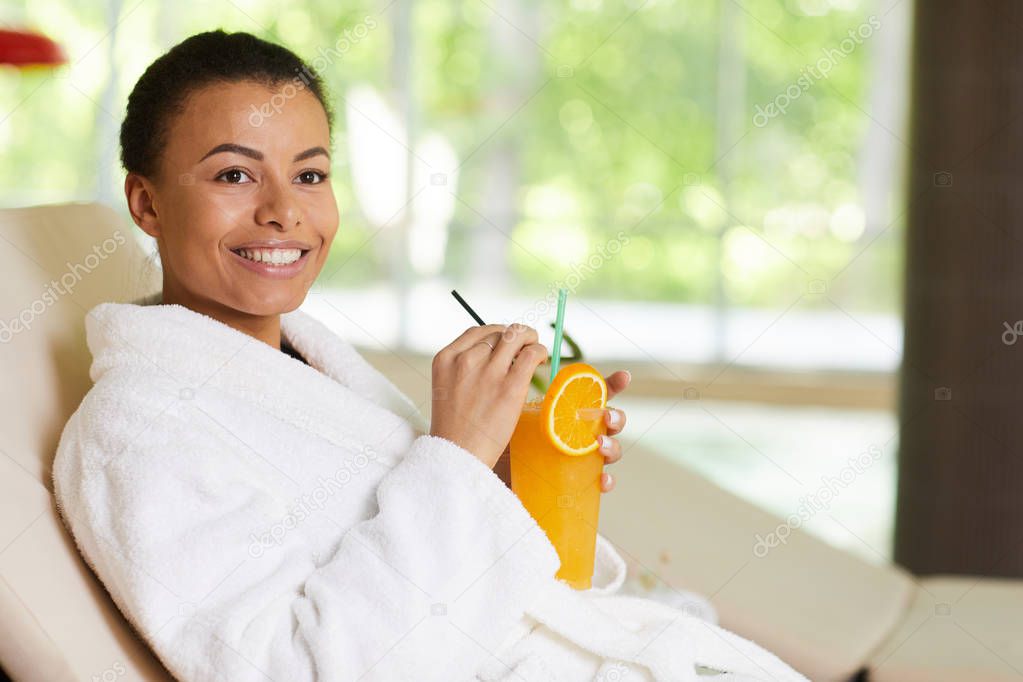 Portrait of beautiful mixed race woman wearing bathrobe relaxing in SPA and drinking cocktail, copy space