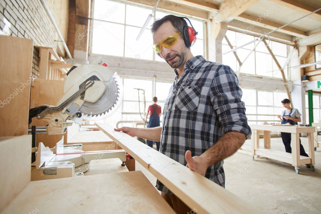 Waist up portrait of mature carpenter sawing wood in industrial workshop, copy space