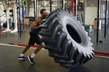 Modern spor salonunda spor yaparken lastiği patlayan kaslı Afro-Amerikan bir adamın tam boy yan görüntüsü.