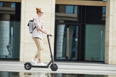 Kentteki işe giderken elektrikli scooter kullanan modern genç bayanın kenar manzarası, boşluğu kopyala