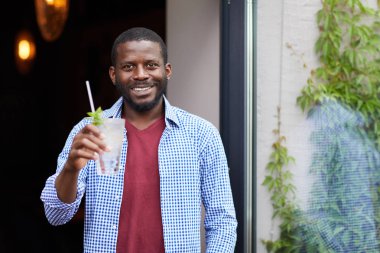 Gülümseyen Afro-Amerikan bir adamın belinde soğuk bir içecek tutarken kafenin yanında poz veren, fotokopi çeken bir adam.