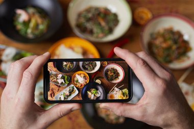 Tanınmayan bir adamın lezzetli Asya yemeklerinin fotoğrafını çekmesini, akıllı telefon ekranına odaklanmasını, uzayı kopyalamasını.