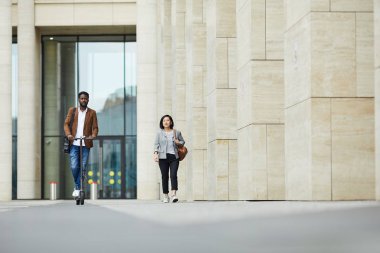 Şehir caddesinde yürüyen iki kişinin tam boy portresi. Elektrikli scooter kullanan Afro-Amerikalı bir adama odaklan.