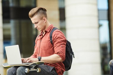 Şehir ortamında çalışırken dizüstü bilgisayar kullanan yakışıklı bir gencin yan görünüm portresi, boşluğu kopyala