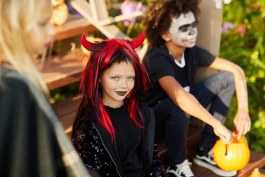 Cadılar Bayramı 'nda çocukların yüksek açılı portresi. Süslü evin merdivenlerinde oturmuş kameraya bakan gülümseyen kız.