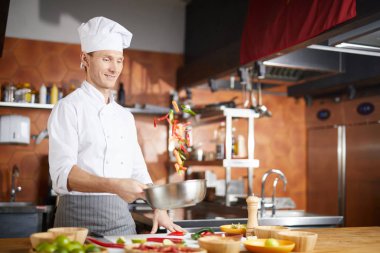 Restoran mutfağında Asya yemeği pişirirken sebze atan yakışıklı bir şefin belden aşağı portresi.