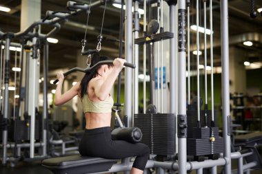 Spor salonunda egzersiz yaparken ağırlık kaldıran formda genç bir kadının arka plan portresi.