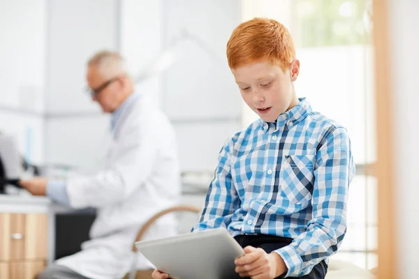 Portret Uroczego Rudego Chłopca Korzystającego Tabletu Cyfrowego Poczekalni Gabinecie Lekarskim — Zdjęcie stockowe