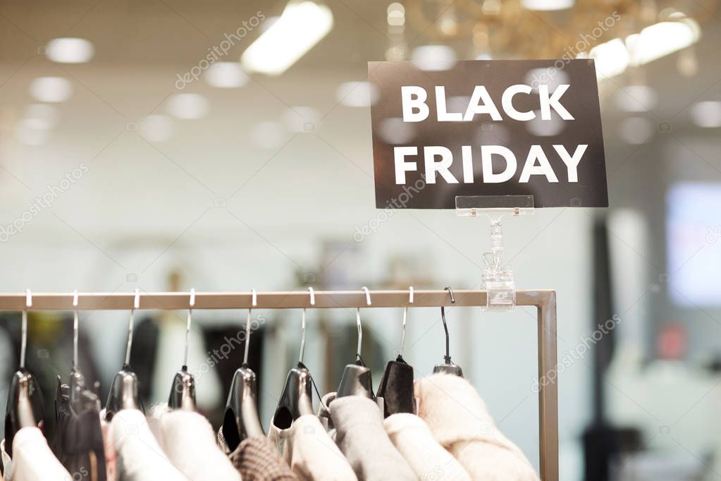 Background image of BLACK FRIDAY sigh in window display above rack with clothes on sale in shopping mall, copy space