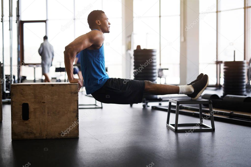 Side view portrait of muscular African-American man doing pull ups on plywood box during cross training in gym, copy space