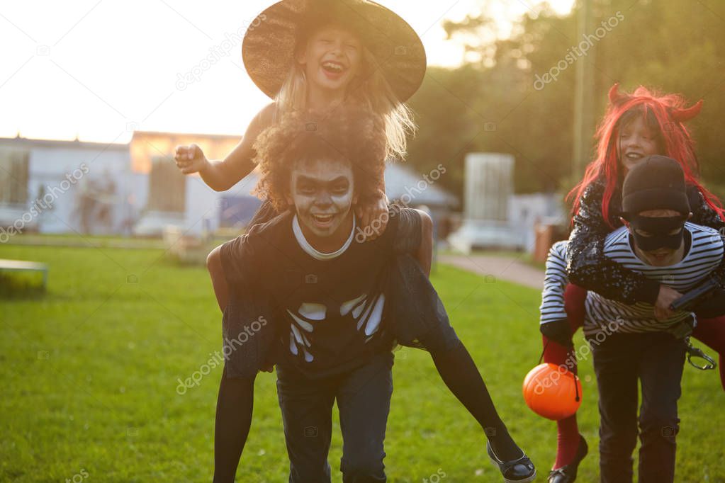 Portrait of carefree kids playing outdoors on Halloween and running towards camera laughing happily