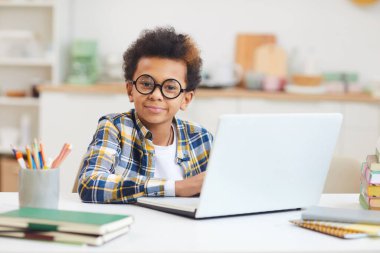 Evde çalışırken laptop kullanan ve büyük gözlük takan yakışıklı Afro-Amerikan çocuk portresi, uzaktan eğitim konsepti, kopyalama alanı
