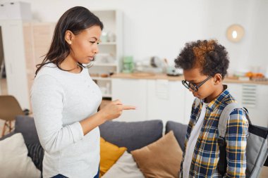 Modern bir apartman dairesinde dururken okulda başarısız olduğu için azarlanan Afro-Amerikalı genç bir kadının yan görüntüsü.