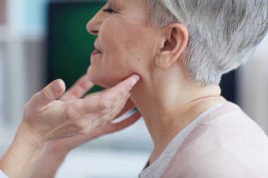 Klinikteki danışmanlık sırasında gülümseyen yaşlı kadını muayene eden tanınmayan kadın doktorlara yakın durun.