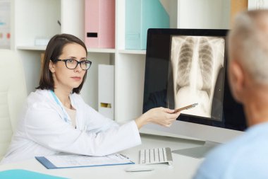 Ciddi bir kadın doktorun portresi klinikteki yaşlı hastaya danışırken akciğer ve göğüs röntgenlerine bakıyor.