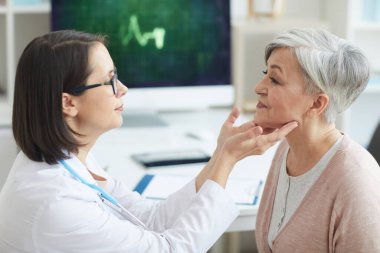 Klinikteki danışmanlık sırasında yaşlı kadını muayene eden kadın doktor portresi.