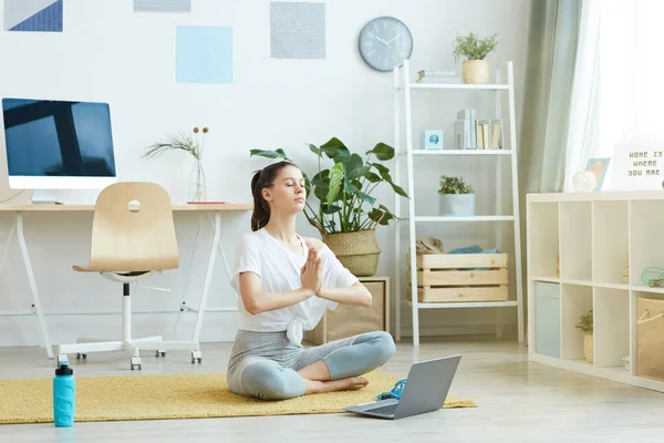 Evdeki Lotus pozisyonunda oturup, uzayı kopyalayarak yoga yapan çağdaş genç kadının tam boy portresi.