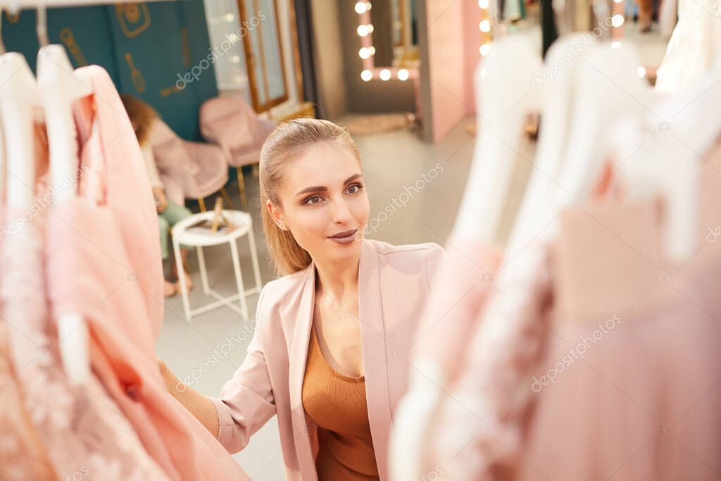 High angle view at glamorous woman choosing dress on rack in clothing boutique, copy space