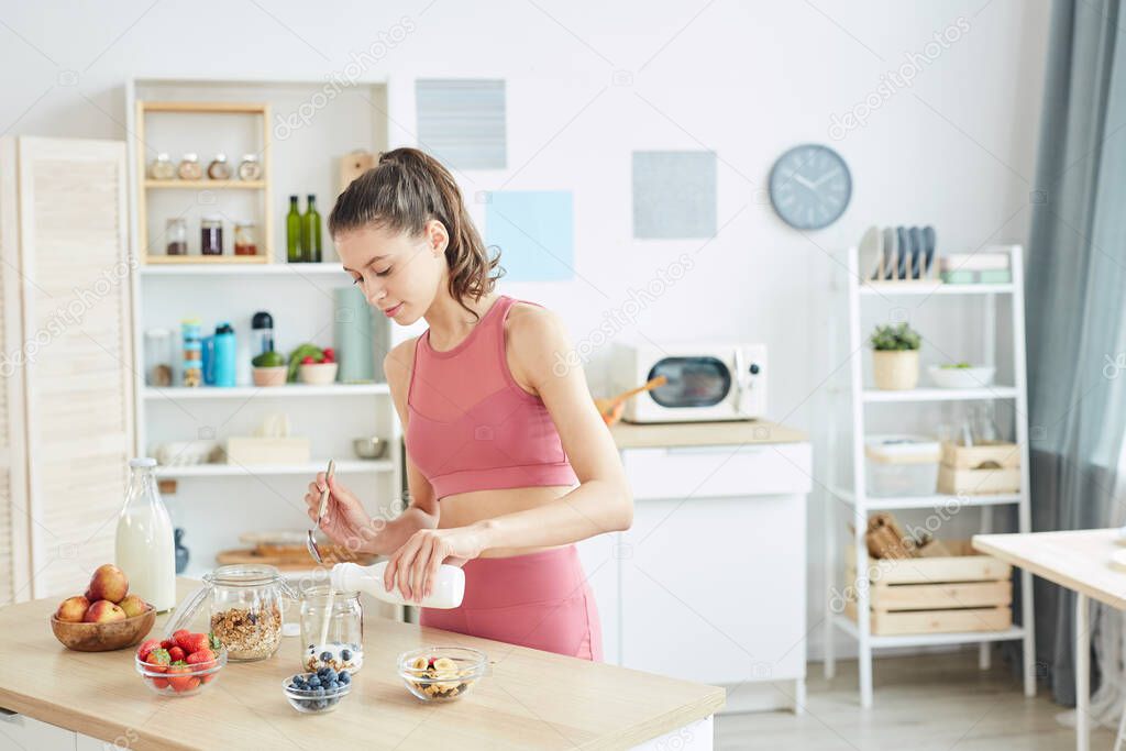 Waist up portrait of fit young woman making healthy granola snack in modern kitchen interior, copy space