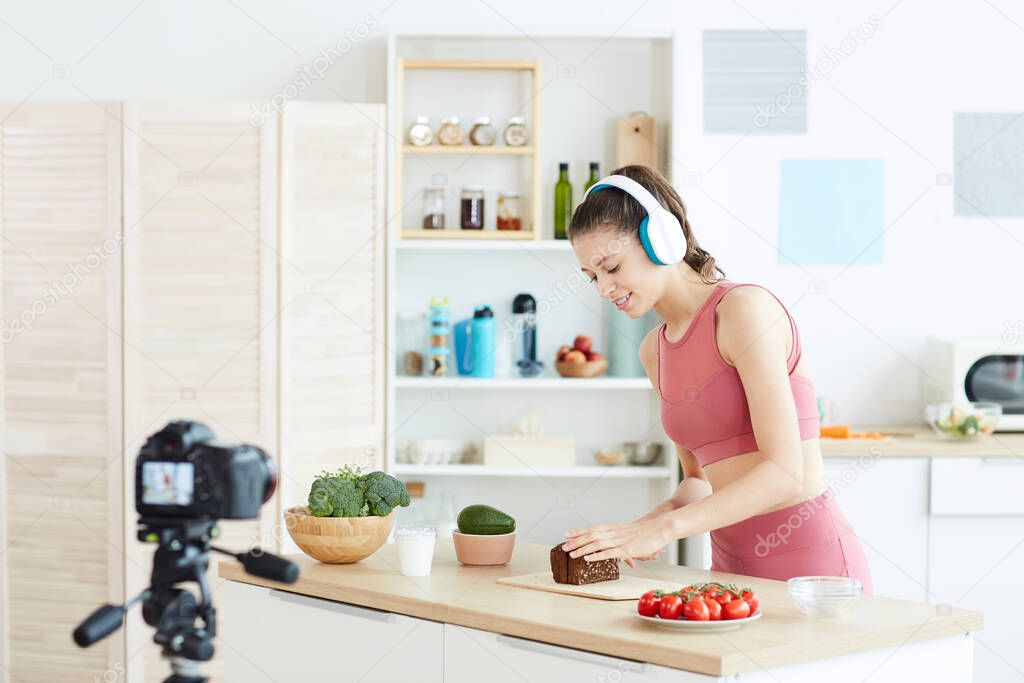 Portrait of young fitness blogger recording cooking video in kitchen interior, copy space