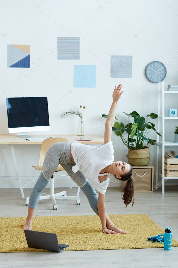 Vertical full length portrait of contemporary young woman doing yoga exercises during fitness workout at home, copy space