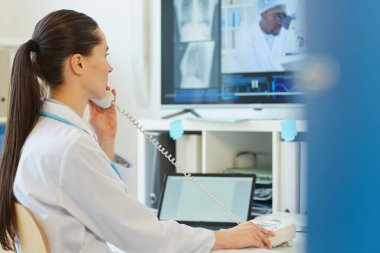 Masada otururken, klinikte ya da hastanede çalışırken telefonla konuşan kadın doktorların yan görüş portresi, boşluğu kopyala