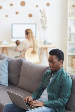 Evlerinden çalışan modern ırklar arası ailenin dikey portresi, önplanda dizüstü bilgisayar kullanan Afrikalı-Amerikalı adama odaklan, uzayı kopyala