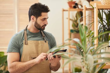 Çiçekçide stok sayarken dijital tablet kullanan yakışıklı sakallı adamın belini kaldırın, boşluğu kopyalayın.