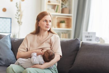 Bebek emziren olgun bir annenin portresi. Evdeki koltukta oturup başka yere bakıyor, boşluğu kopyalıyor.