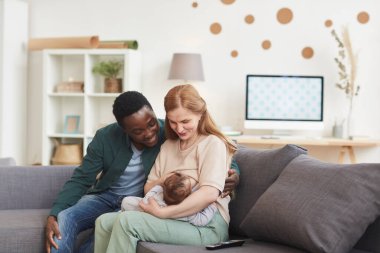 Mutlu ırklar arası bir ailenin portresi evde koltukta oturan olgun bir anne tarafından emzirilen bebek, kopyalama alanı.