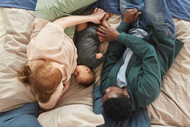 Irklar arası aile portresinin yukarısında, evde rahat bir yatakta uzanan şirin bir bebek, boşluğu taklit ediyor.