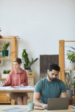 Ofisteki ahşap masada çalışırken dizüstü bilgisayar kullanan modern sakallı adamın dikey portresi, boşluğu kopyala