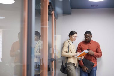 İki çağdaş ofis çalışanının belden yukarı portresi. Salonda duvara yaslanırken belgeleri tartışıyorlar. Boşluğu kopyala.