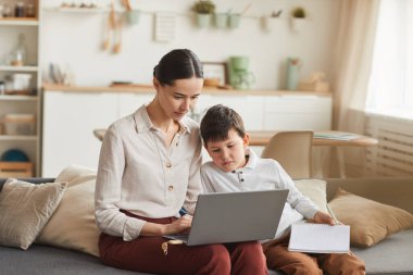 Samimi iç mekanda çalışırken dizüstü bilgisayar kullanan zarif anne ve oğulun sıcak tonlu portresi, boşluğu kopyala